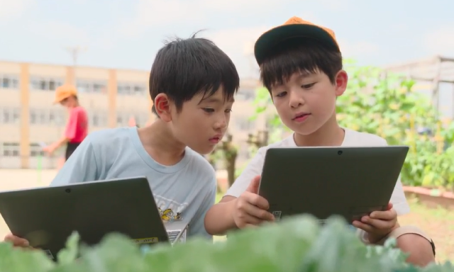 画像：一人一台ずつパソコンを持ち画面をのぞきながら話をする二人の男子生徒