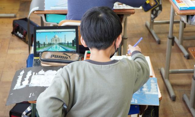 画像：パソコンの中の写真を見ながら絵を描く男子生徒の後ろ姿