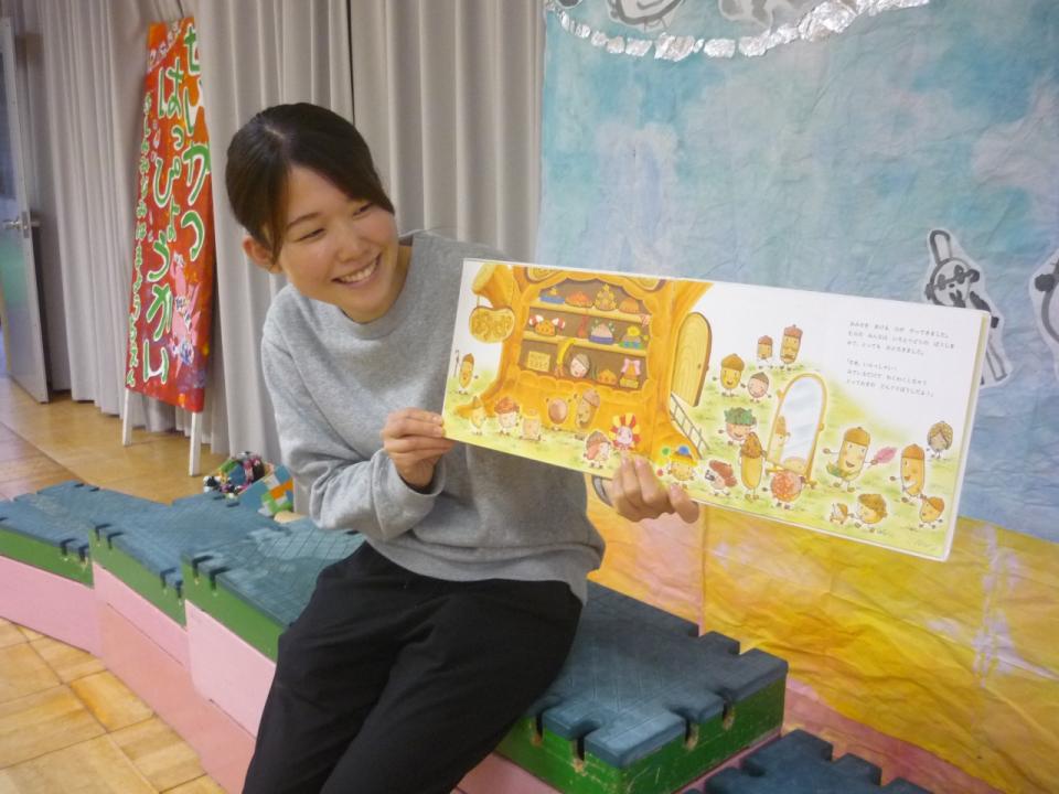 写真：カーテンの前で絵本を読む笑顔の先生3